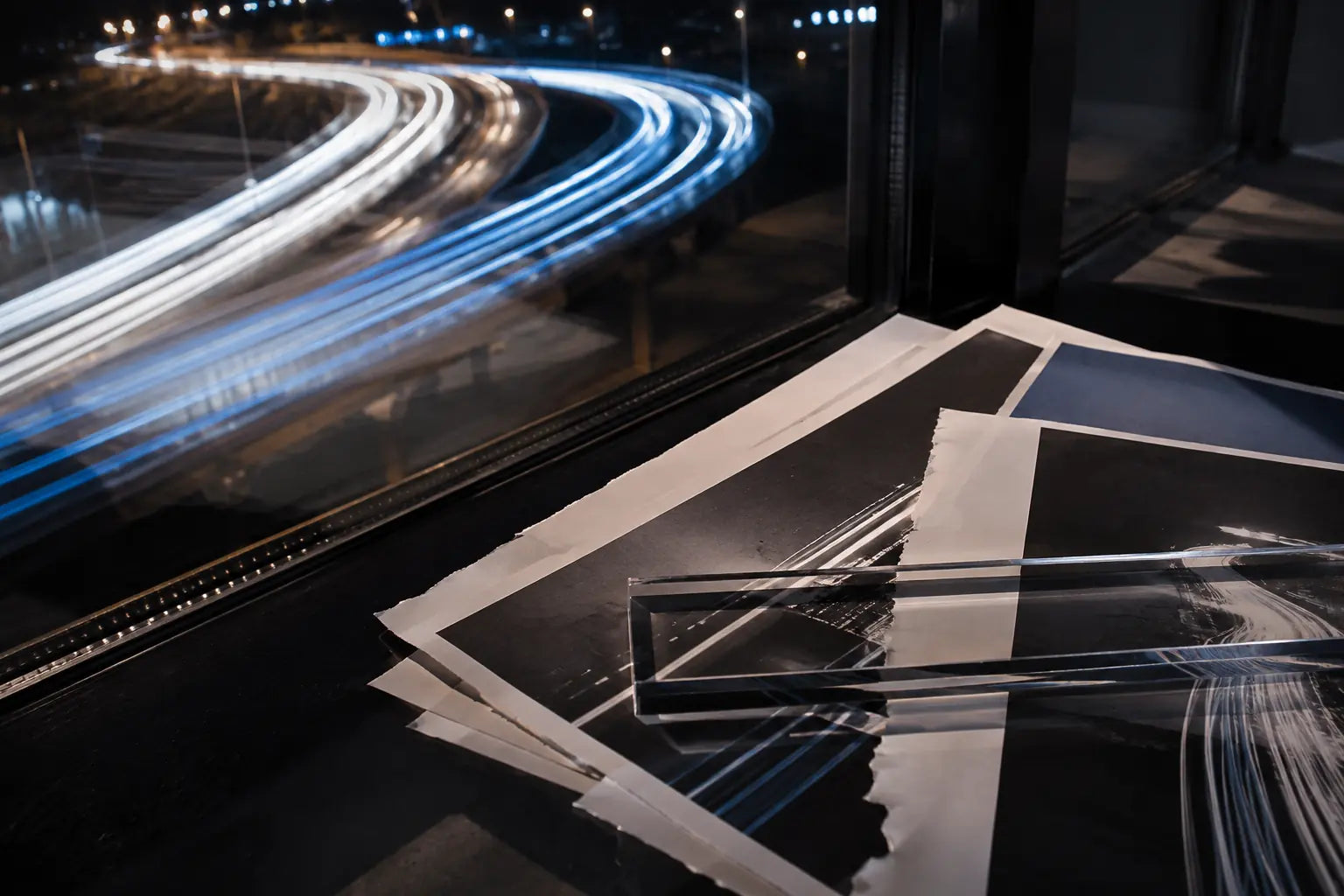 Long-exposure highway light trails crossing torn print proofs and an acrylic ruler